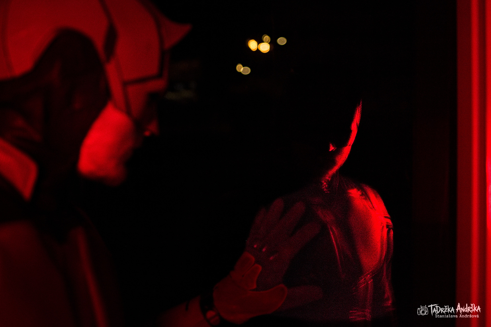 csopaly daredevila, ze tmy se rýsují jen rudé siluety osvícené červeným světlem, v o draze černého skla se rýsuje druhá polovina siluety se světly města v pozadí.